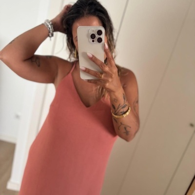 Pessoa a tirar selfie com vestido cor de rosa e pulseiras, em interior com chão de madeira e armário branco