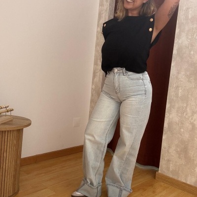 Mulher com calças de ganga largas, t-shirt preta e sapatos cinza e branco num ambiente interior