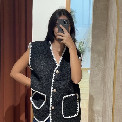 Colete preto tufado com bordas brancas e botões castanhos com bolsos frontais