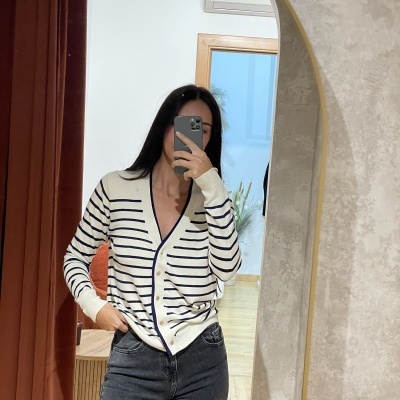 Mulher a vestir camisola cardigan riscada e jeans, tirando selfie num espelho