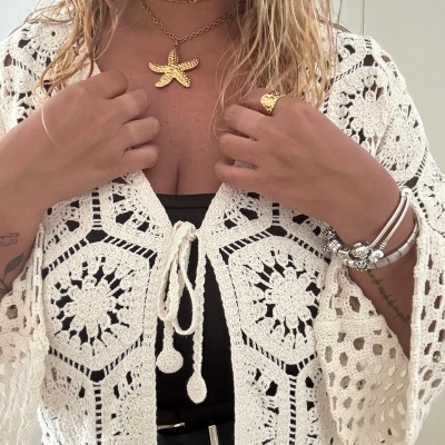 Mulher com top de croché branco de padrão floral, colar dourado de estrela do mar e pulseiras prateadas
