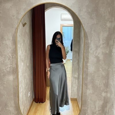 Mulher a tirar selfie em espelho oval com top preto e saia comprida cinza prateada.