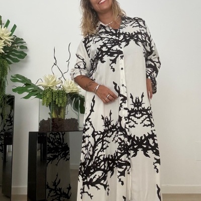 Vestido preto e branco com padrão abstrato em mulher sorridente, planta em vaso preto ao lado