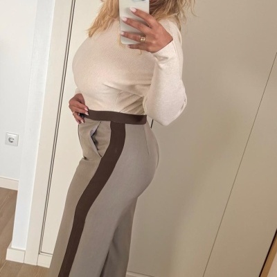 Calças cinza com faixa castanha laterais e cinto, usadas por mulher com camisola creme em divisão interior.