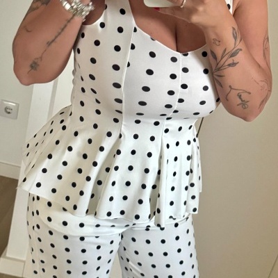 Conjunto de roupa branco de bolinhas pretas com top e calças, tatuagens nos braços e unhas vermelhas