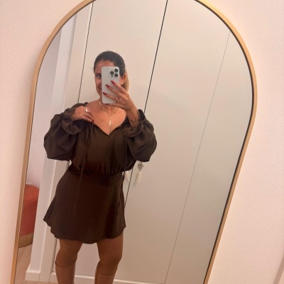 Mulher a tirar selfie num espelho usando vestido castanho escuro e botas castanhas.