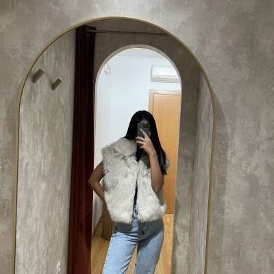 Pessoa em colete de pêlo branco tirando selfie em espelho com moldura dourada