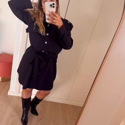 Pessoa a tirar selfie vestindo vestido preto e botas pretas em frente a um espelho