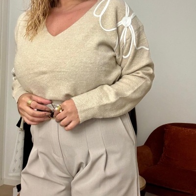 Mulher com camisola bege de malha com bordado branco e calças largas bege claro com cinto castanho