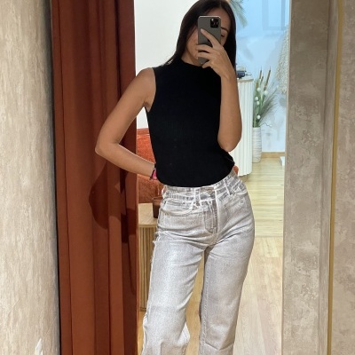 Mulher com camisola preta sem mangas e calças de ganga claras a tirar selfie num espelho