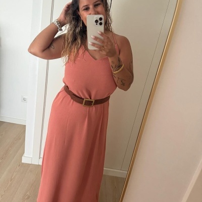 Vestido comprido rosa salmão com cinto castanho e sandálias bege em interior com chão de madeira.