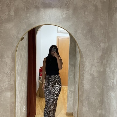 Pessoa a usar blusa preta e saia lápis padrão animal print a tirar foto num espelho oval com moldura dourada