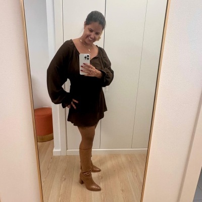 Mulher a tirar selfie com vestido castanho e botas castanhas em frente a um espelho grande.