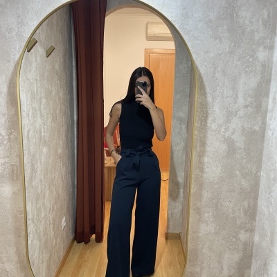 Espelho oval dourado com mulher a tirar selfie vestindo roupa preta em parede cinzenta texturada