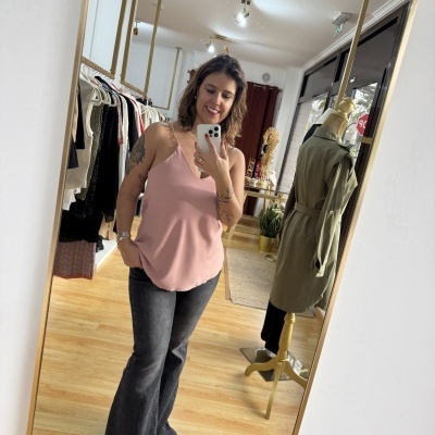 Mulher com blusa rosa e calças pretas em loja de roupas com manequim e cabides ao fundo