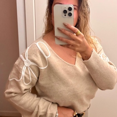 Camisola bege com flor branca nas mangas e decote em V vista num espelho