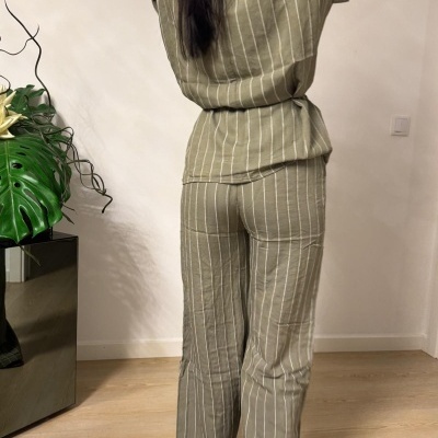 Conjunto de pijama bege com riscas brancas visto de costas em ambiente interior.