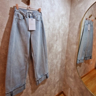 Calças de ganga azuis claras penduradas numa parede cinzenta com etiqueta CAMELIA