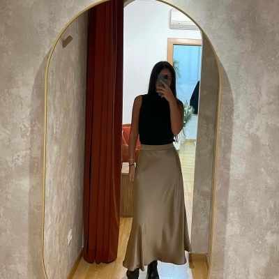 Mulher a tirar selfie num espelho com top preto, saia castanha clara e botas pretas em interior