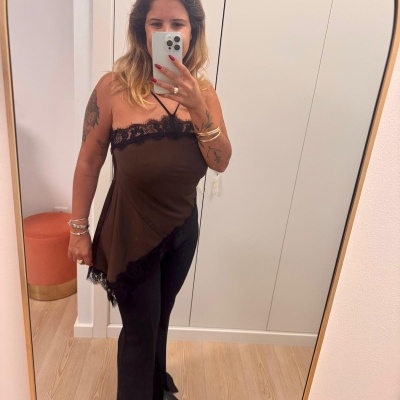 Mulher com top castanho com renda preta e calças pretas a tirar selfie num espelho