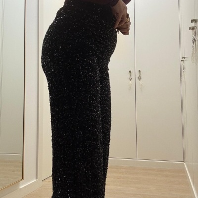 Calças pretas com lantejoulas brilhantes usadas por pessoa em quarto com chão de madeira