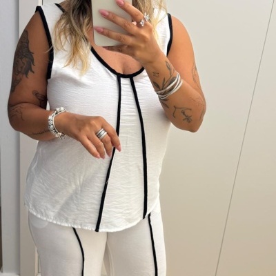 Mulher com conjunto branco com linhas pretas a tirar selfie em espelho em ambiente interior