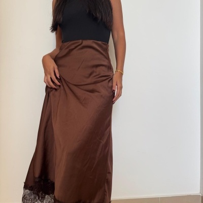 Saia castanha acetinada com renda preta na bainha usada por mulher com top preto