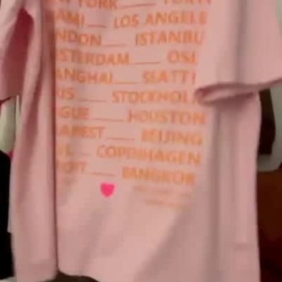 T-shirt cor-de-rosa com ICONIC em rosa e nomes de cidades em letras laranja.