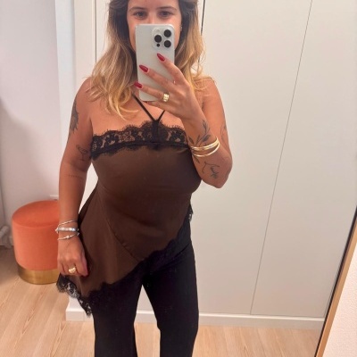 Mulher com camisola castanha com renda preta e calças pretas em espelho