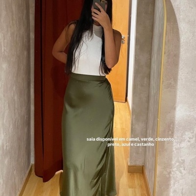 Saia verde acetinada com pregas na barra e top branco num ambiente interior