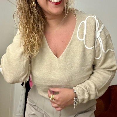 Pessoa com suéter bege de malha com detalhe em linha branca e calças beje.