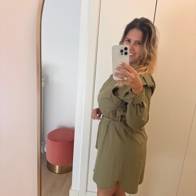 Mulher a tirar selfie em frente a espelho usando vestido verde-oliva com cinto e botas pretas.
