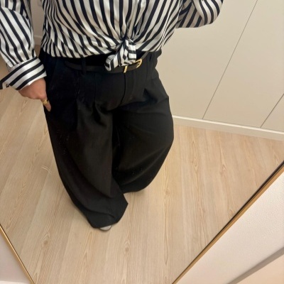 Pessoa com camisa riscada preta e branca e calças largas pretas em frente a espelho