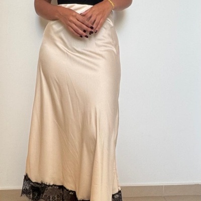 Mulher vestindo top preto, saia de cetim creme com renda preta e chinelos creme