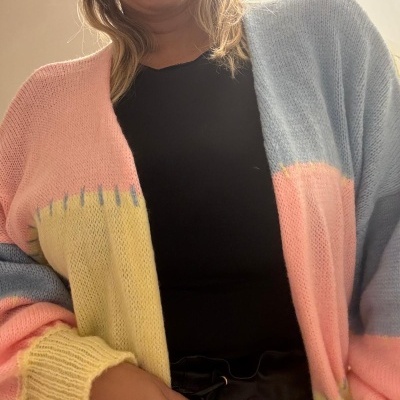 Cardigan de malha colorido azul, rosa e amarelo numa pessoa com t-shirt e calças pretas