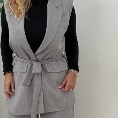 Mulher com colete cinzento riscado, calças largas cinzentas e camisola preta em fundo branco