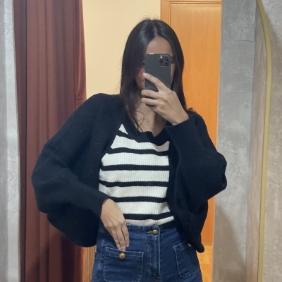 Pessoa com camisola às riscas e casaco preto a tirar selfie diante de um espelho num quarto