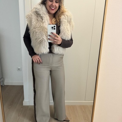 Mulher com colete de pêlo bege claro e calças largas bege em selfie no espelho