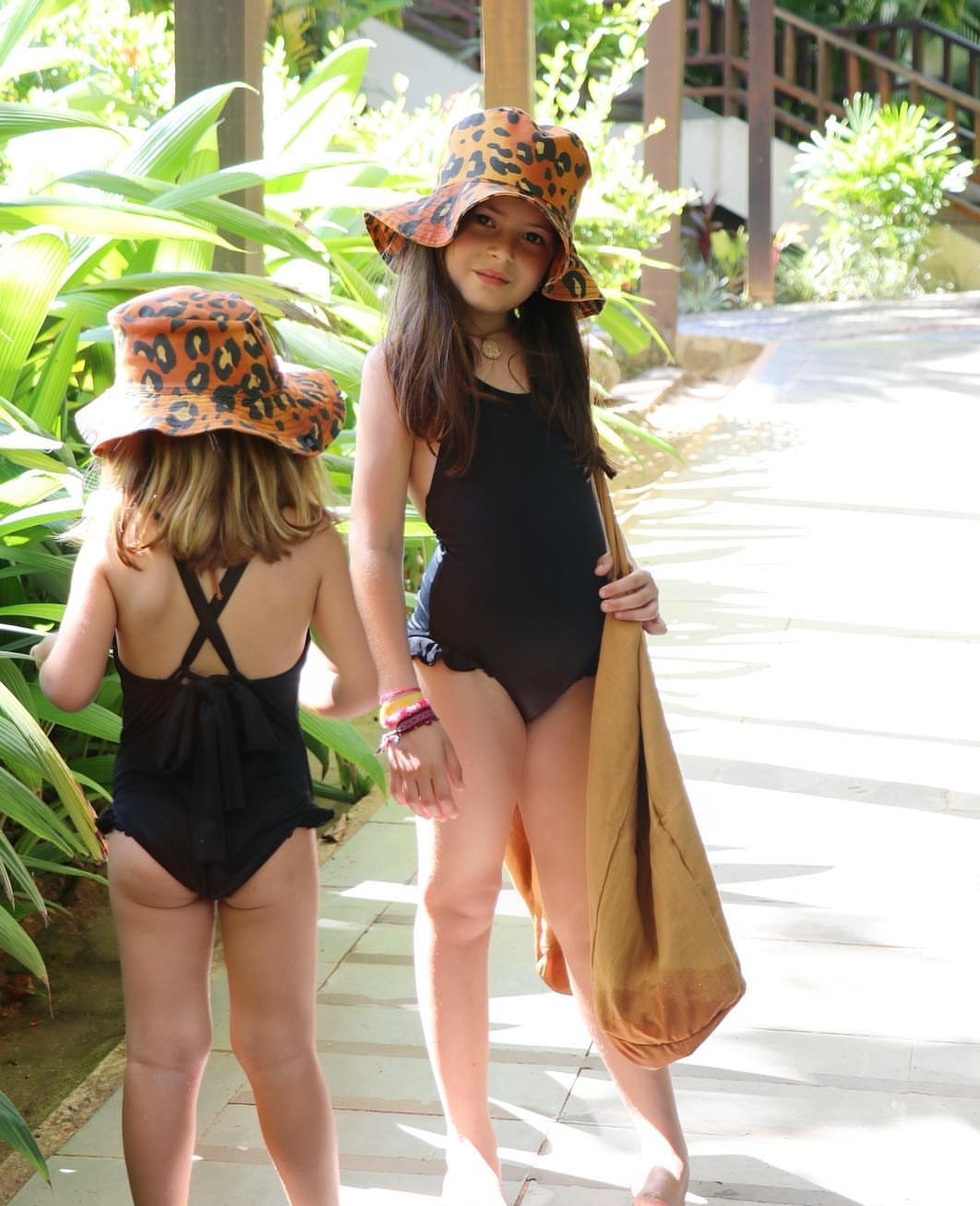 Duas raparigas em fatos de banho pretos e chapéus animal print laranja e preto na rua