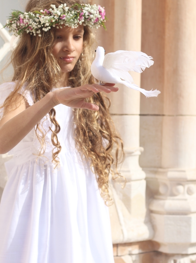 Menina de vestido branco com coroa de flores segurando uma pomba branca com asas abertas