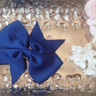 Laço de cabelo azul escuro em tecido sobre bandeja metálica texturizada com flores brancas e rosa ao lado