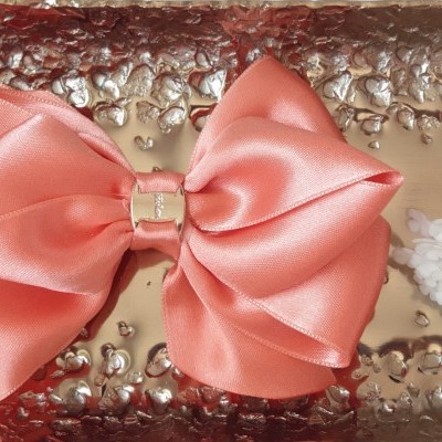 Laço de cabelo coral em cetim com elo dourado em superfície dourada texturada e flores ao lado