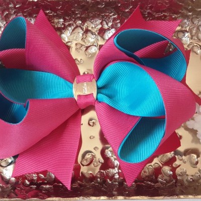 Laço de cabelo azul-turquesa e vermelho-rosado sobre bandeja dourada com flores brancas