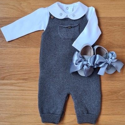Conjunto bebé com camisola branca, jardineira cinzenta de malha e sapatos cinzentos com laços.
