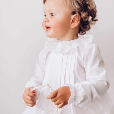 Criança vestindo blusa branca com gola de renda segurando colar de pérolas