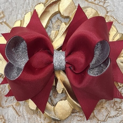 Laço de cabelo vermelho com detalhes prateados sobre fundo texturizado dourado e bege