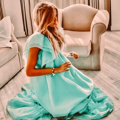 Mulher com vestido azul claro sentada no chão ao lado de poltrona e sofá