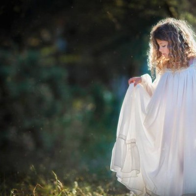 Criança com vestido branco longo em ambiente natural ao ar livre.