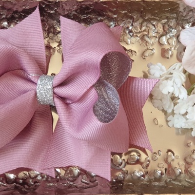 Laço rosa com centro prateado em bandeja dourada texturizada e flores rosa e branca ao lado
