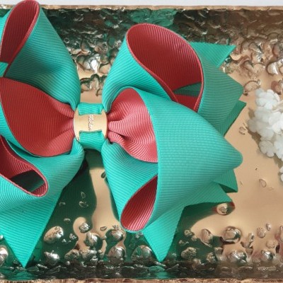 Laço verde azulado e vermelho numa bandeja metálica com flores ao lado